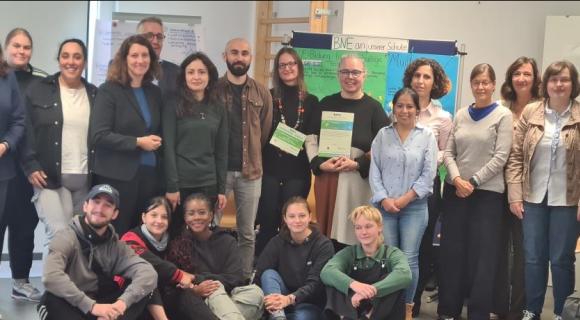 von links: Dr. Julia Boger (WUS), Nina Rathmann, Berna Semtürk; Dr. Dorothea Kliche-Behnke (MdL), Achim Beule (KM), Nicole Villanueva, Oshur Ozodi (WUS), Janine Dietrich, Dagmar Schön-Luetkens (Schulleitung IB-Tübingen), N. Condori (WUS), Lela Kerklishvili, Iris Heinz, Barbara Wäcker, Silvia Herbsthofer.  Vordere Reihe von links: Linus Schunn, Sarah Riecken, Rosa Da Cresta, Luisa Grul, Lugh Eber. © S. Kowitzke 2024 Eine Gruppe von 20 Personen steht in einem Raum und hält Zertifikate in den Händen. Einige Personen in der Mitte übergeben ein Zertifikat an eine andere. Der Hintergrund zeigt ein Plakat zum Thema „BNE an unserer Schule“ (Bildung für nachhaltige Entwicklung). Die Gruppe ist vielfältig in Bezug auf Geschlecht und Herkunft, und die Atmosphäre wirkt freundlich und engagiert. Alle Personen lächeln, und es scheint sich um eine feierliche Übergabe oder Auszeichnung zu handeln.